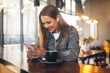 Woman in coffee shop listening to music from cell phone