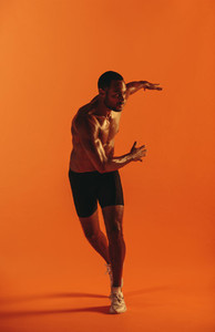 Muscular athlete working out on orange background