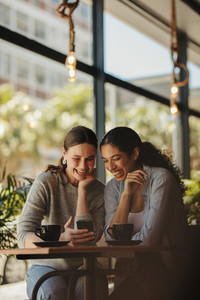 Friends looking at phone and smiling in coffee shop