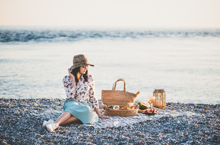 Young woman having picnic at sunset at seaside with appetizers