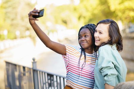Two multiethnic female friends making selfie outdoors