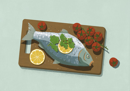 Whole cooked fish with lemons and tomatoes on cutting board