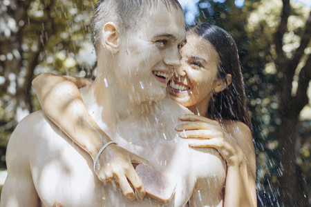 Happy young couple with soap showering outdoors
