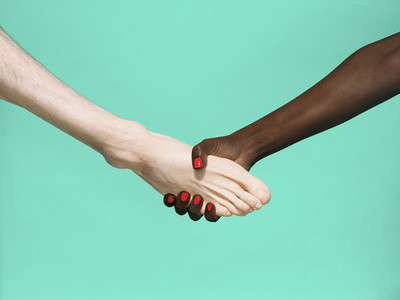 Multiethnic foot and hand shake on green background