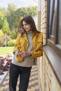 Beautiful young woman in yellow jacket outside house