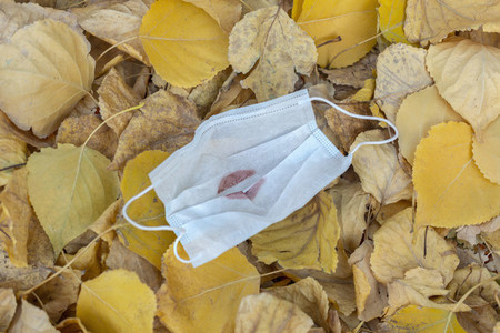 Lipstick kiss on protective face mask in heap of yellow autumn leaves