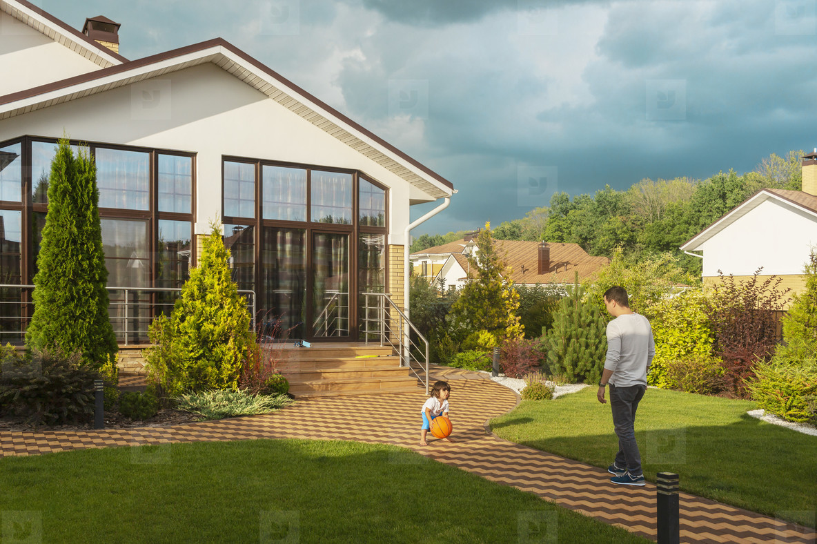Father and toddler son playing with basketball in sunny backyard