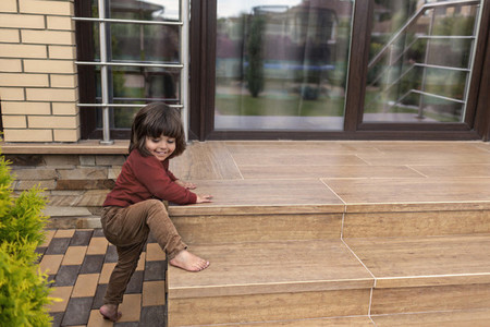 Cute barefoot toddler boy climbing patio steps