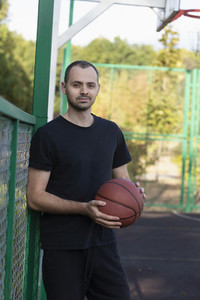 Portrait confident young man playing basketball at park basketball court