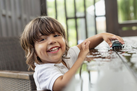 Portrait happy with cute toddler boy playing with toy car on wet patio table
