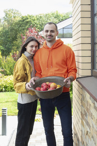 Portrait happy young couple with bowl of fresh harvested apples