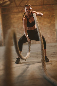Tough woman working out with battle rope in old warehouse