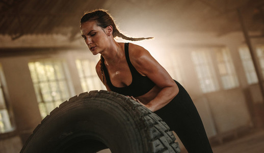 Strong woman doing tire flip workout at old warehouse