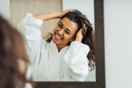 Happy brunette woman with palms in her hair looking at mirror reflection