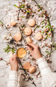 Womans hands holding fresh coffee over macaron cookies and flowers