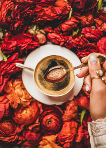 Womans hand holding spoon of espresso coffee over red flowers