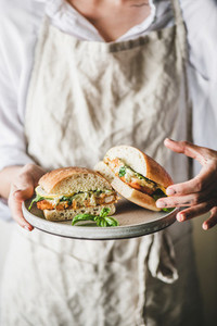 Woman holding plate with fresh fried fish sandwich in halves