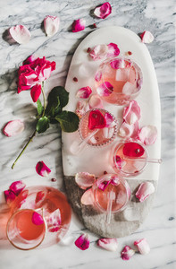 Rose lemonade with ice and rose petals over marble background