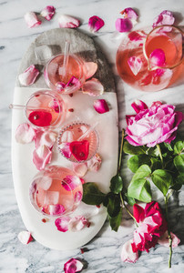 Rose lemonade with ice and fresh roses over marble background