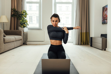Young woman repeating exercises while watching online exercise session on her laptop