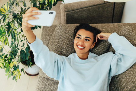 Beautiful happy woman lying on a sofa in a living room a taking selfie