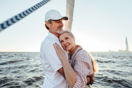 Mature husband and wife embracing each other at sunset on the yacht  Senior woman with her head on husbands chest looking away