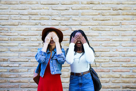 Two female friends covering their eyes outdoors Multiethnic women