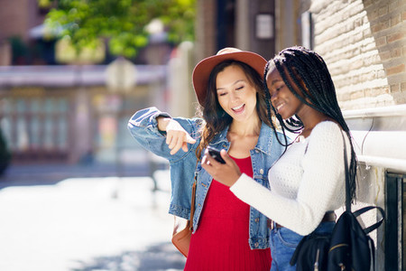 Two friends looking at their smartphone together Multiethnic women