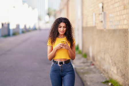 Young Arab woman walking in the street using her smartphone