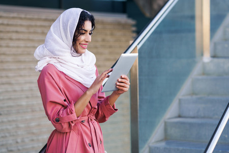 Young Muslim woman wearing hijab using digital tablet outdoors