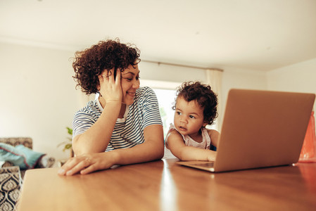 Mother watching baby pretending working on laptop