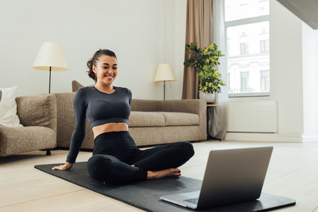 Smiling woman in sportswear sitting on a mat in the living room