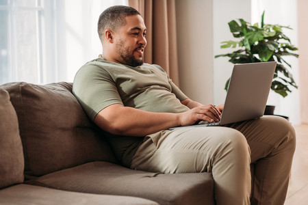 Smiling man with laptop on his hips sitting on a sofa