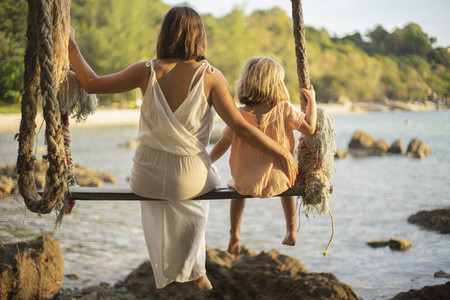 Mother and daughter on large rope swing over ocean