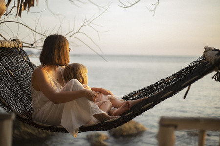 Serene mother and daughter in hammock enjoying ocean sunset