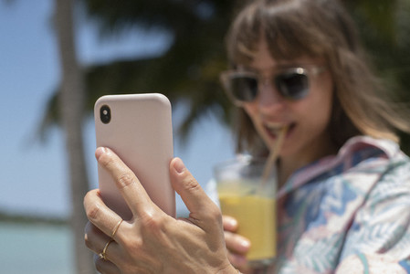 Woman with smart phone sipping cocktail on sunny beach