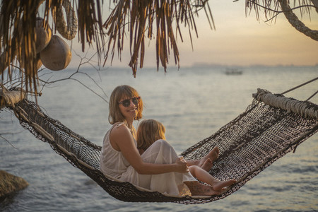 Portrait mother and daughter in hammock enjoying ocean sunset