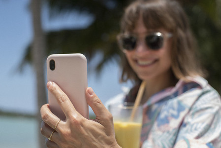 Happy woman with cocktail taking selfie on sunny beach
