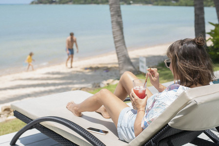 Woman enjoying cocktail on sunny beach lounge chair
