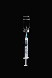 Syringe in COVID 19 vaccine vial on black background