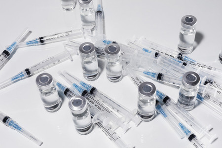 Syringes and COVID 19 vaccine vials on white background