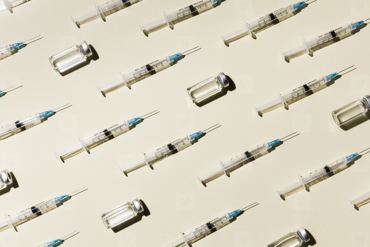 COVID-19 vaccine syringes and vials on yellow background