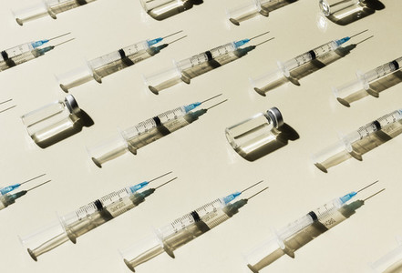 Syringes and COVID 19 vaccine vials on yellow background