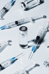 Syringes around COVID 19 vaccine vial on white background