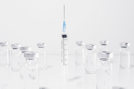 COVID 19 vaccine vials surrounding syringe on white background