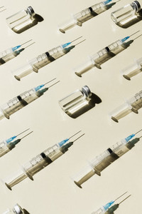 Syringes and COVID 19 vaccine vials on yellow background