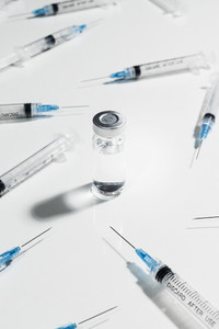 Syringes surrounding COVID 19 vaccine vial on white background