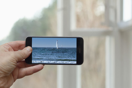 POV Person looking at photo of sailboat and ocean on smart phone screen