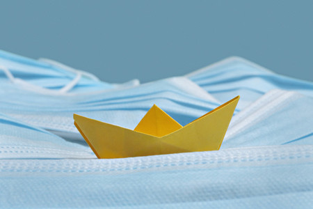 Yellow origami boat on disposable blue face masks