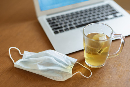 Protective face mask and tea at laptop
